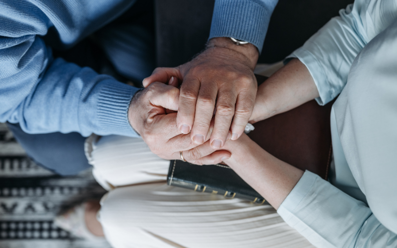 two people holding hands over a bible doing grief coaching